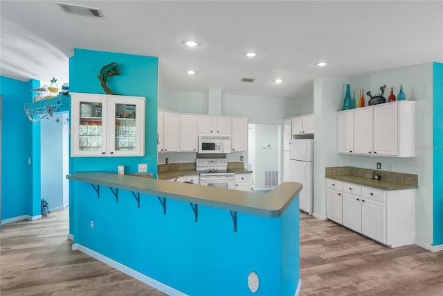 kitchen featuring a breakfast bar, white cabinetry, light wood-type flooring, and white appliances