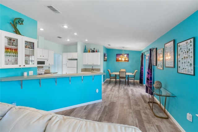 kitchen featuring pendant lighting, white appliances, light hardwood / wood-style floors, a breakfast bar area, and white cabinets