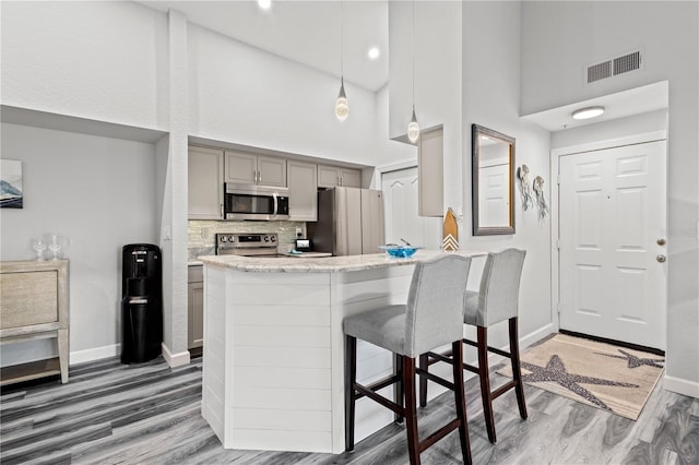 kitchen with appliances with stainless steel finishes, a kitchen breakfast bar, decorative light fixtures, a high ceiling, and gray cabinets