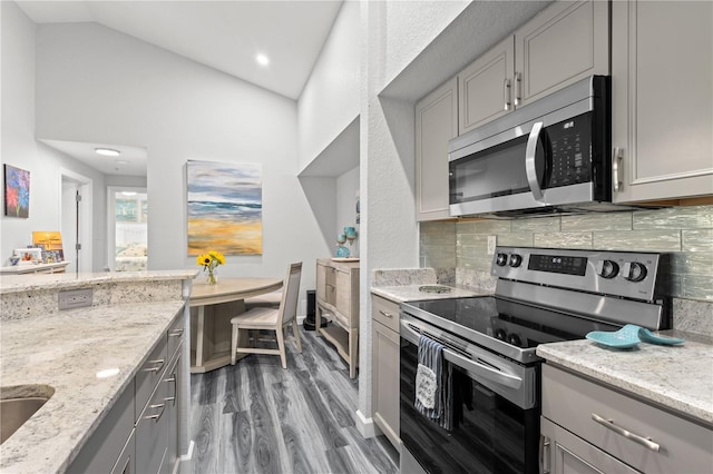 kitchen featuring decorative backsplash, gray cabinets, dark hardwood / wood-style floors, light stone counters, and stainless steel appliances