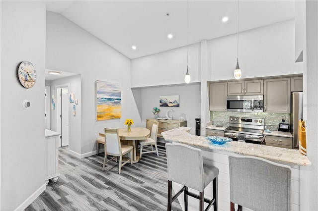 kitchen featuring a kitchen bar, appliances with stainless steel finishes, tasteful backsplash, decorative light fixtures, and high vaulted ceiling