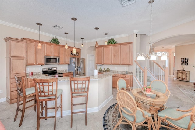 kitchen featuring hanging light fixtures, light stone counters, a textured ceiling, a center island with sink, and appliances with stainless steel finishes