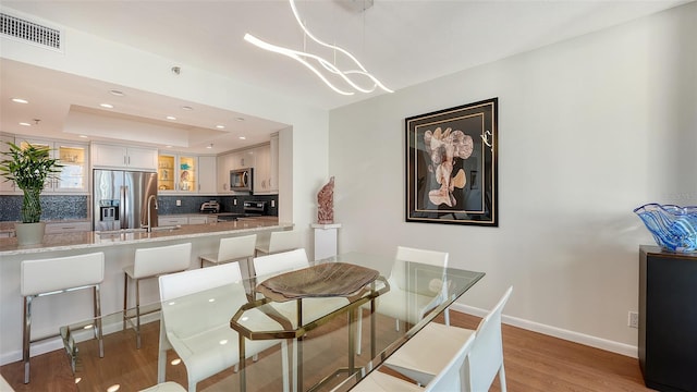 dining room featuring a tray ceiling, sink, a notable chandelier, and light wood-type flooring