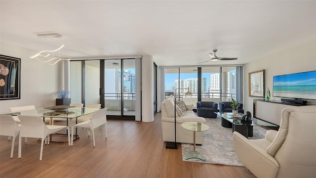 living room featuring ceiling fan with notable chandelier, light hardwood / wood-style floors, and a wall of windows