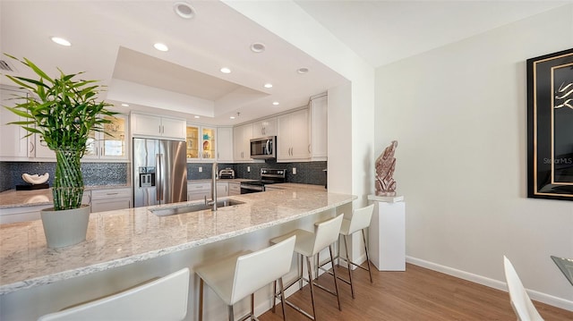 kitchen with white cabinetry, sink, light stone counters, appliances with stainless steel finishes, and light wood-type flooring