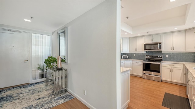 kitchen featuring appliances with stainless steel finishes, tasteful backsplash, a tray ceiling, light hardwood / wood-style flooring, and white cabinetry