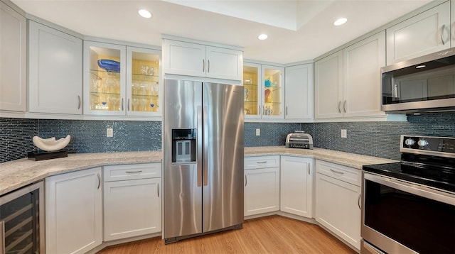 kitchen featuring white cabinets, light hardwood / wood-style floors, light stone countertops, and stainless steel appliances