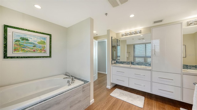 bathroom with hardwood / wood-style floors, vanity, and a relaxing tiled tub