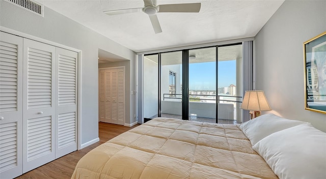 bedroom with access to outside, two closets, ceiling fan, a wall of windows, and hardwood / wood-style floors