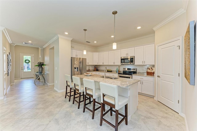 kitchen with light stone countertops, stainless steel appliances, a kitchen island with sink, sink, and white cabinets