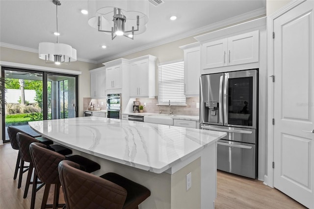 kitchen featuring appliances with stainless steel finishes, a kitchen breakfast bar, sink, white cabinetry, and hanging light fixtures