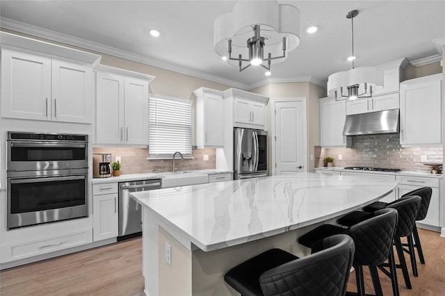 kitchen featuring decorative light fixtures, stainless steel appliances, a kitchen island, and white cabinetry