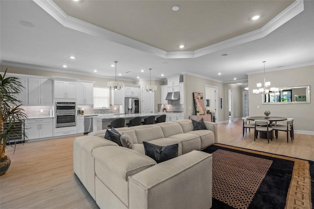 living room with an inviting chandelier, sink, crown molding, a tray ceiling, and light hardwood / wood-style floors