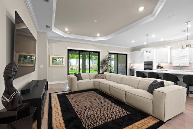 living room featuring a raised ceiling, light hardwood / wood-style flooring, crown molding, and sink