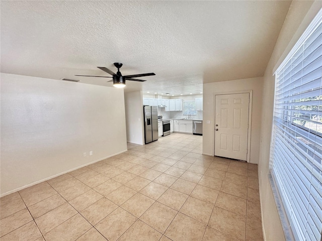 unfurnished living room with ceiling fan, sink, light tile patterned floors, and a textured ceiling