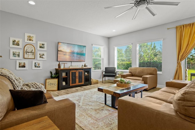 living room featuring ceiling fan, light hardwood / wood-style flooring, and a textured ceiling