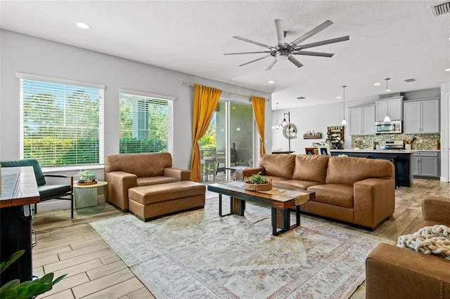 living room with ceiling fan, a textured ceiling, and light hardwood / wood-style flooring