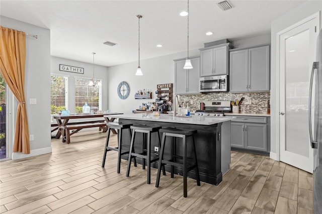 kitchen with appliances with stainless steel finishes, a breakfast bar, a kitchen island with sink, pendant lighting, and gray cabinets