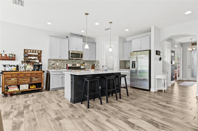 kitchen featuring appliances with stainless steel finishes, light wood-type flooring, a kitchen island with sink, pendant lighting, and a breakfast bar area