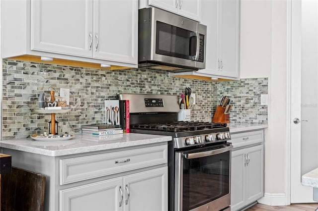 kitchen with decorative backsplash, white cabinets, light stone countertops, and appliances with stainless steel finishes