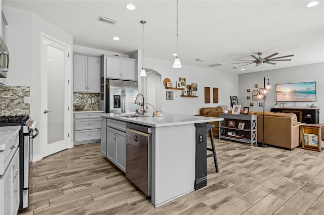 kitchen featuring a center island with sink, gray cabinetry, stainless steel appliances, and hanging light fixtures