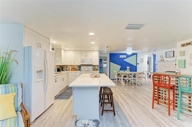 kitchen with a kitchen breakfast bar, light wood-type flooring, white appliances, a kitchen island, and white cabinetry