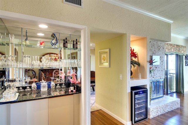 bar with dark stone counters, crown molding, beverage cooler, and dark hardwood / wood-style floors