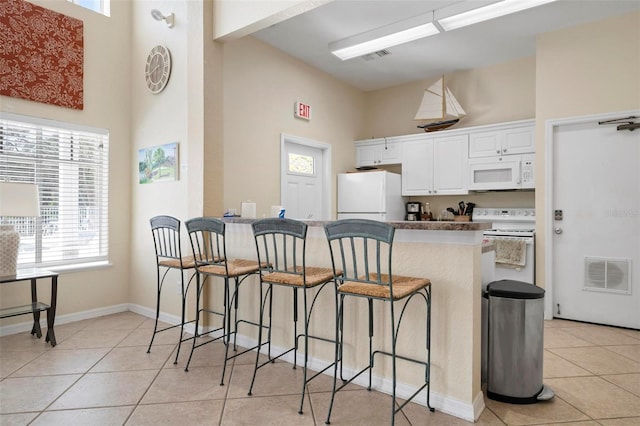 kitchen with light tile patterned floors, white appliances, a breakfast bar, and white cabinets