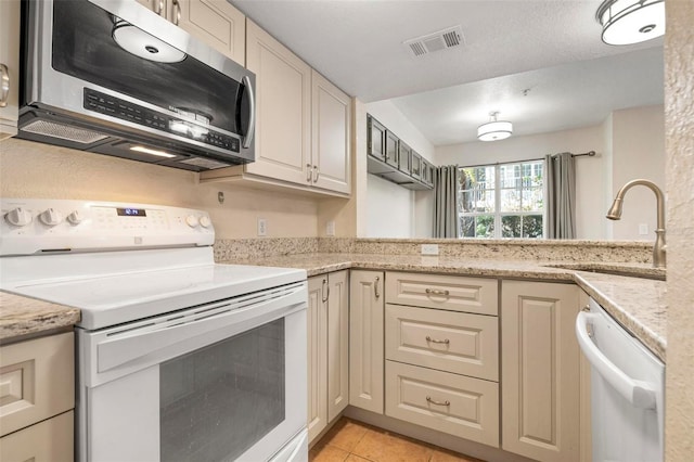 kitchen with white appliances, cream cabinets, sink, light tile patterned flooring, and light stone counters