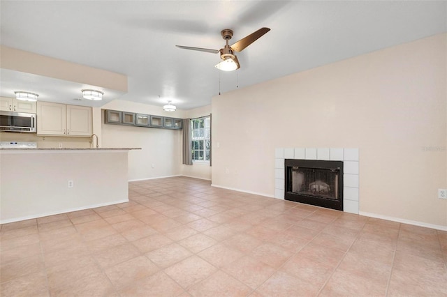 unfurnished living room with a tiled fireplace and ceiling fan