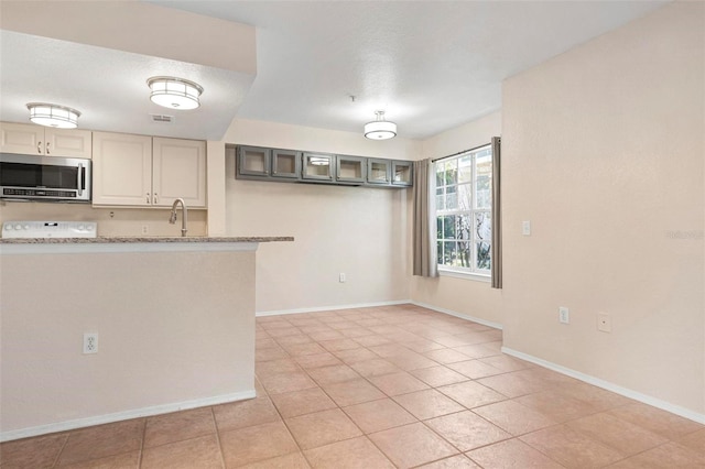 kitchen featuring light stone counters, stove, sink, and light tile patterned floors