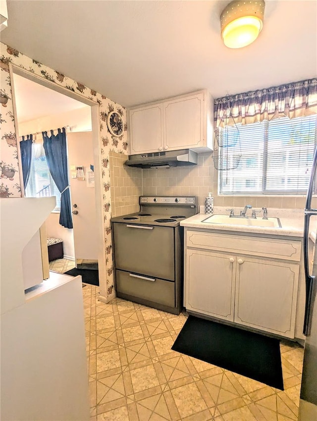 2228 Canal Dr Unit D26, Bradenton, FL 34207 - kitchen featuring electric stove, under cabinet range hood, wallpapered walls, white cabinetry, and freestanding refrigerator