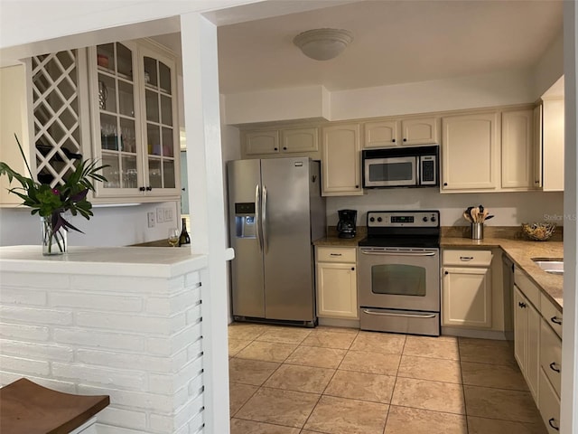 kitchen with cream cabinets, light tile patterned floors, and appliances with stainless steel finishes