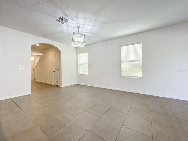 tiled spare room with a chandelier and a textured ceiling