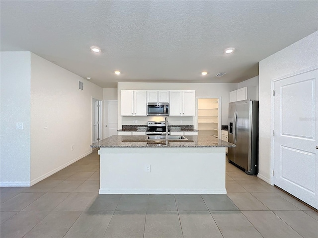 kitchen with dark stone countertops, white cabinetry, a kitchen island with sink, and appliances with stainless steel finishes