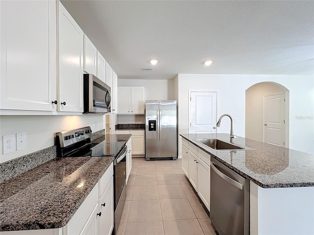 kitchen with dark stone counters, a center island with sink, sink, appliances with stainless steel finishes, and white cabinetry