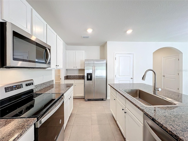 kitchen with white cabinetry, sink, dark stone counters, light tile patterned floors, and appliances with stainless steel finishes