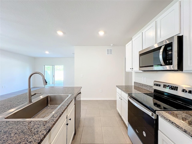 kitchen with dark stone counters, sink, light tile patterned floors, appliances with stainless steel finishes, and white cabinetry