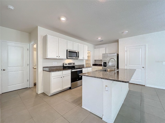 kitchen with appliances with stainless steel finishes, light tile patterned floors, a center island with sink, and white cabinetry