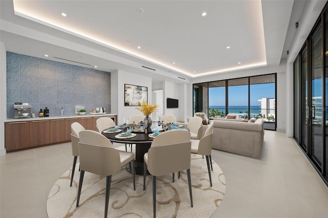 dining space with sink, light tile patterned floors, tile walls, and a tray ceiling