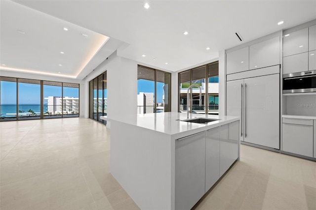 kitchen with paneled built in fridge, a water view, sink, an island with sink, and a wall of windows