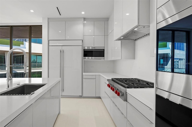 kitchen featuring paneled fridge, stainless steel gas cooktop, sink, wall chimney range hood, and white cabinets