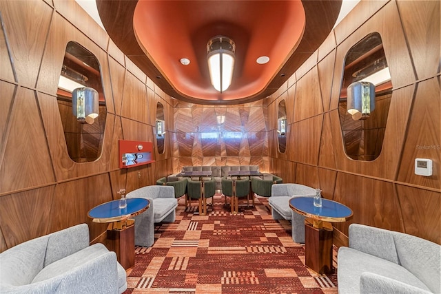 recreation room featuring a tray ceiling, wood walls, and dark colored carpet