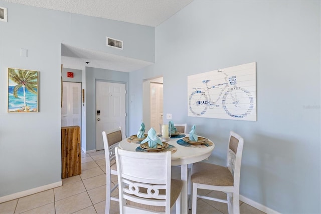 dining area featuring light tile patterned floors, a high ceiling, and a textured ceiling