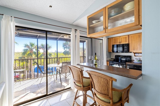 kitchen with a breakfast bar, light tile patterned floors, black appliances, and a textured ceiling