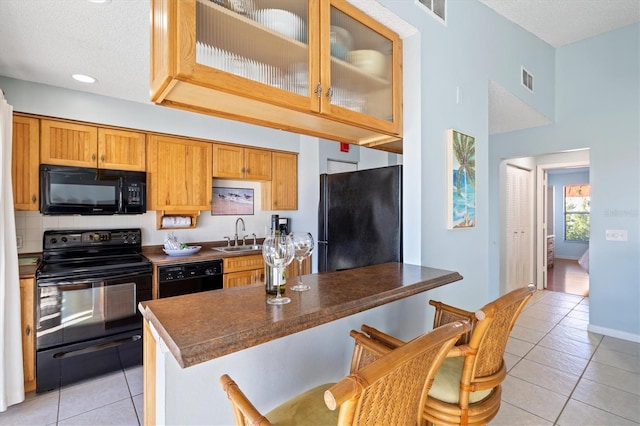 kitchen featuring black appliances, sink, light tile patterned floors, a textured ceiling, and a kitchen bar