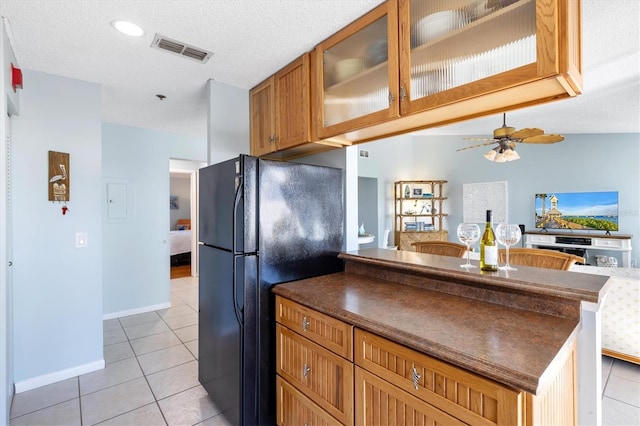 kitchen featuring ceiling fan, black refrigerator, light tile patterned floors, and a textured ceiling