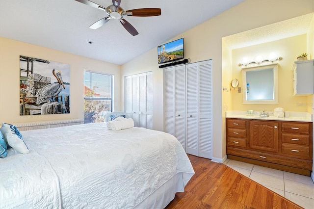 bedroom with light wood-type flooring, two closets, vaulted ceiling, ceiling fan, and connected bathroom