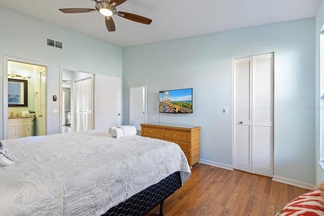 bedroom featuring connected bathroom, hardwood / wood-style flooring, ceiling fan, and multiple closets