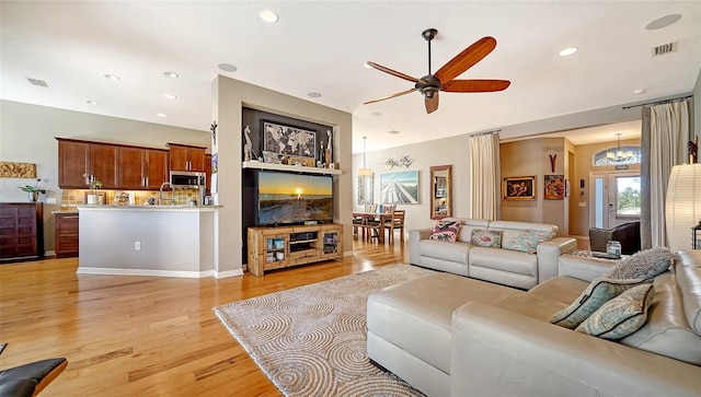 living room with light hardwood / wood-style flooring, ceiling fan with notable chandelier, and sink